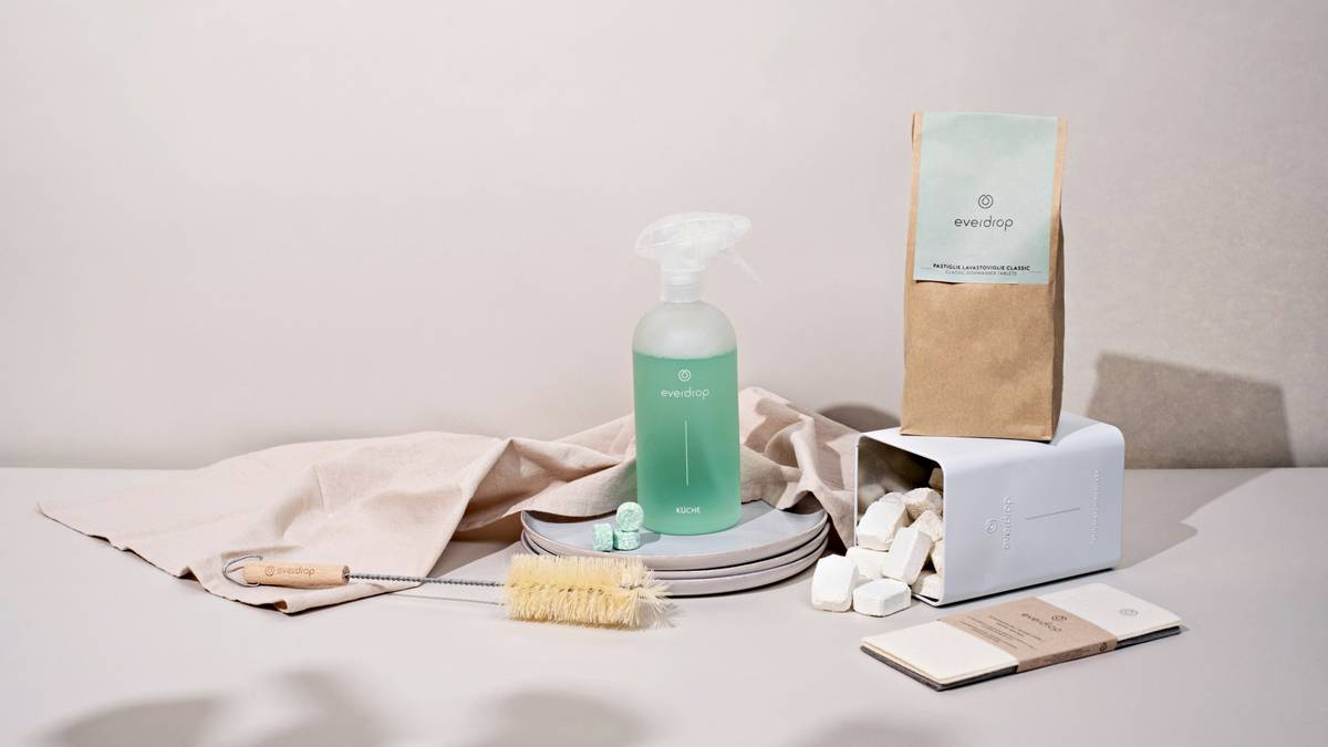 Woman using natural mop pads to clean kitchen tiles with reusable spray bottle nearby